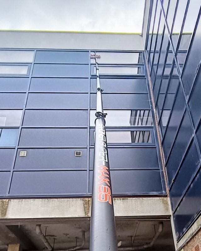 A water fed pole reaching up a commercial building, its brush against the top floor glass panels